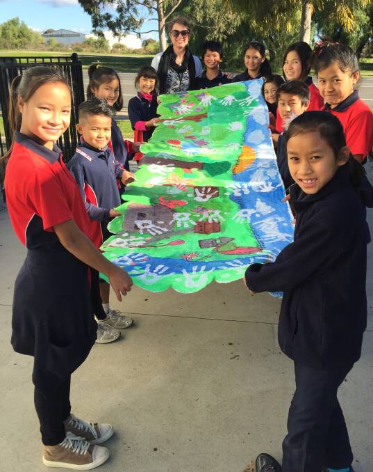 SNAPSHOT OF HOME: Lightning Reef Primary School's Karen students stand in front of a banner they painted of the land they left behind – it depicits elephants, butterflies, lotus flowers and a long line of people holding hands. 