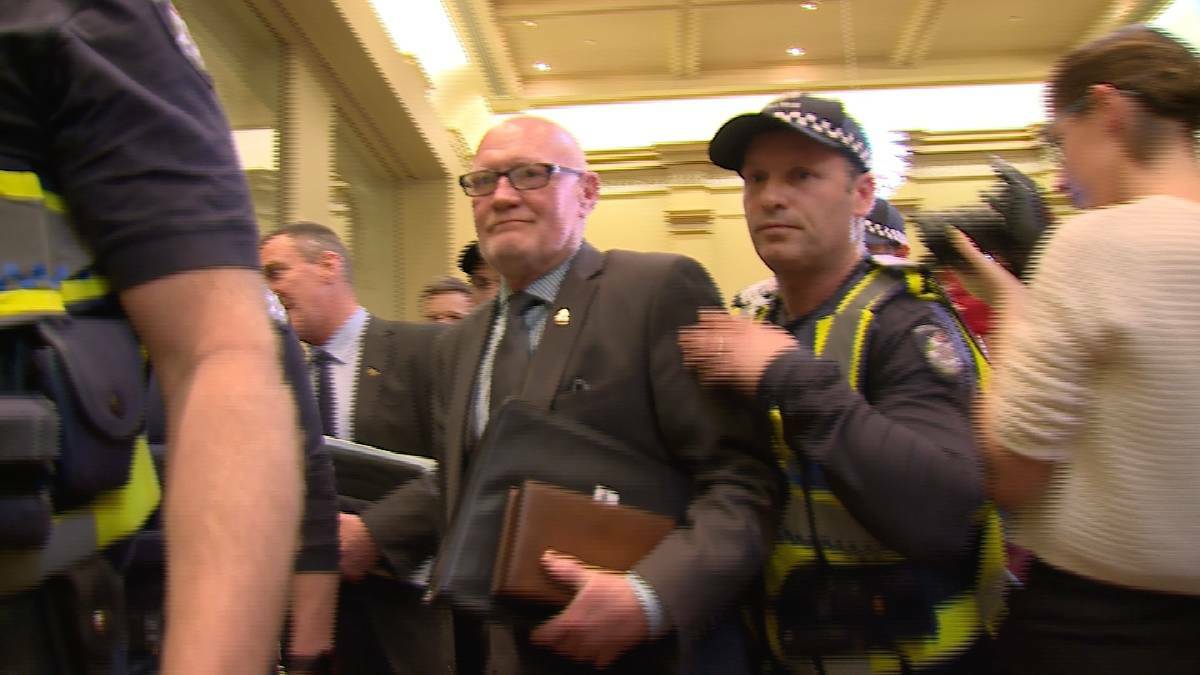 Mayor Peter Cox is escorted from council chambers by police after protesters forced him to cancel the last Bendigo City Council meeting. 