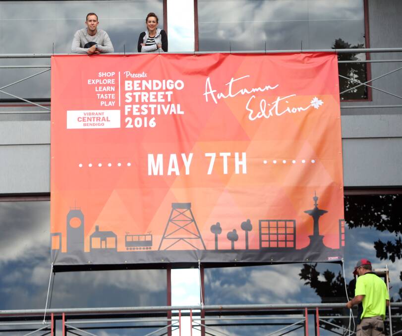 FUN TIMES: Tim Connors and Fi Rooke, of Vibrant Central Bendigo, unfurl a banner at the Bendigo Bank to promote this weekend's street festival. Picture: GLENN DANIELS