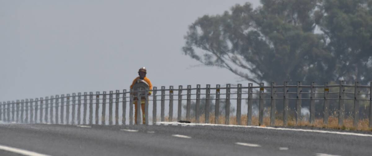 WATER: A firefighter carrying a hose during Sunday's grass fire is pictured behind the wire rope barriers on the Calder Highway. Picture: NONI HYETT