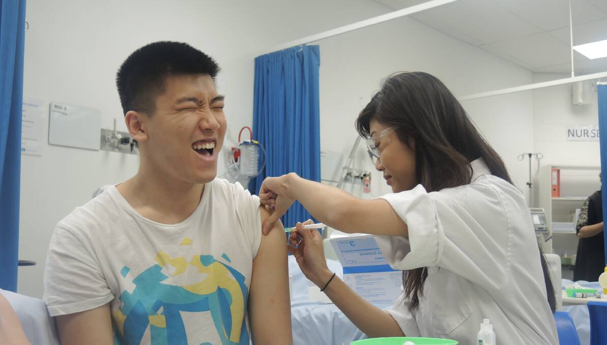 OUCH: Brenda Nguyen delivers her first ever injection to final-year pharmacy classmate Anthony Vu. Picture: MARK KEARNEY