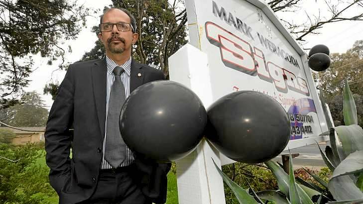 Councillor Mark Weregoda standing next to his business sign, to which protesters affixed black balloons. Photo: Justin McManus