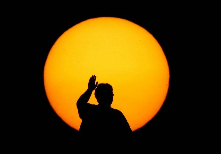 A woman is silhouetted by the setting sun as she waves to passing motorists below Monday, Sept. 11, 2017, to remember the anniversary of the Sept. 11, 2001, terrorist attacks from an overpass on Interstate 35, near Melvern, Kan. Area residents began manning the bridge with flags and waving to motorists on the anniversary in 2002 and have done it every since drawing about 300 people throughout the day. (AP Photo/Charlie Riedel)