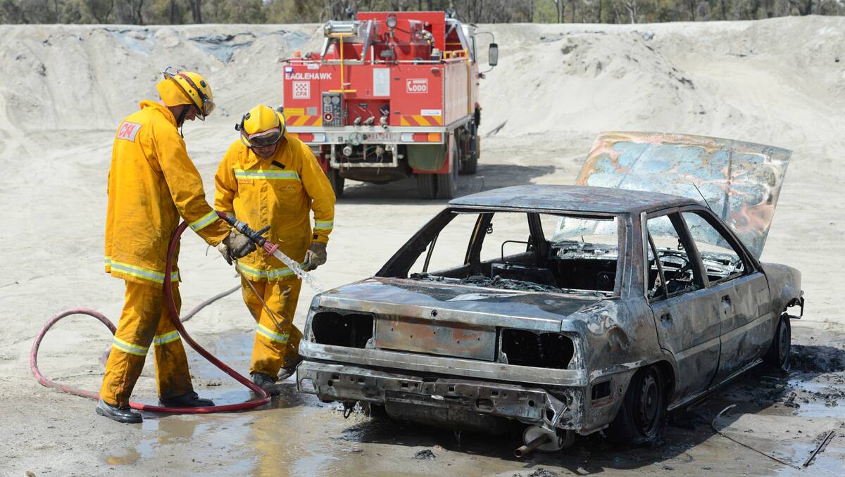 Abandoned: CFA members hose down the torched wreck behind Sailors Gully Road. Picture: Jim Aldersey
