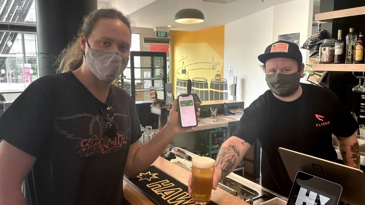 CHEERS: Alex Zegelin, 27, shows off his vaccination certificate while he enjoys a beer at Hustler with restaurant owner Justin McPhail. Picture: CHRIS PEDLER