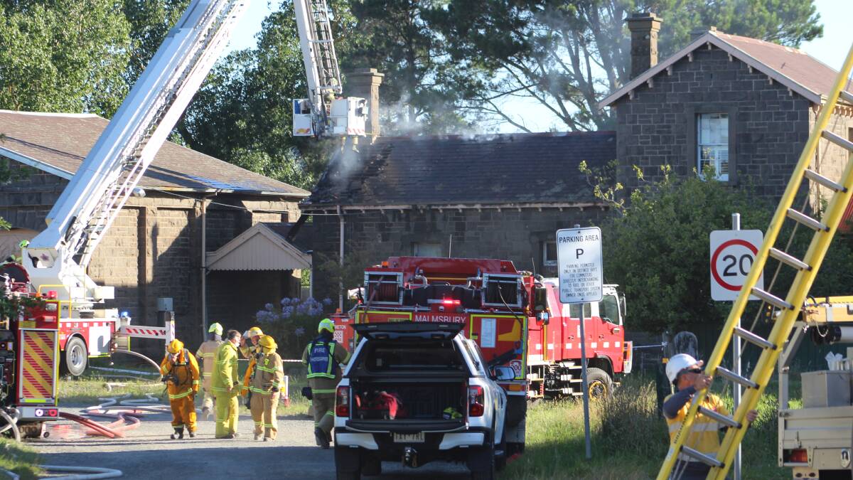 Firefighters work on a ladder platform to douse the still smoking roof of the stationmaster's house at Malmsbury.