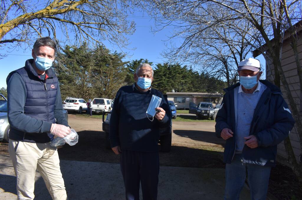 MASKS ON: All attendees at the sale were required to wear face masks. Here Kyneton saleyards manager Terry Fitzpatrick hands out masks to Kieran Keogh, Castlemaine, and Peter Shaw, Carlsruhe.