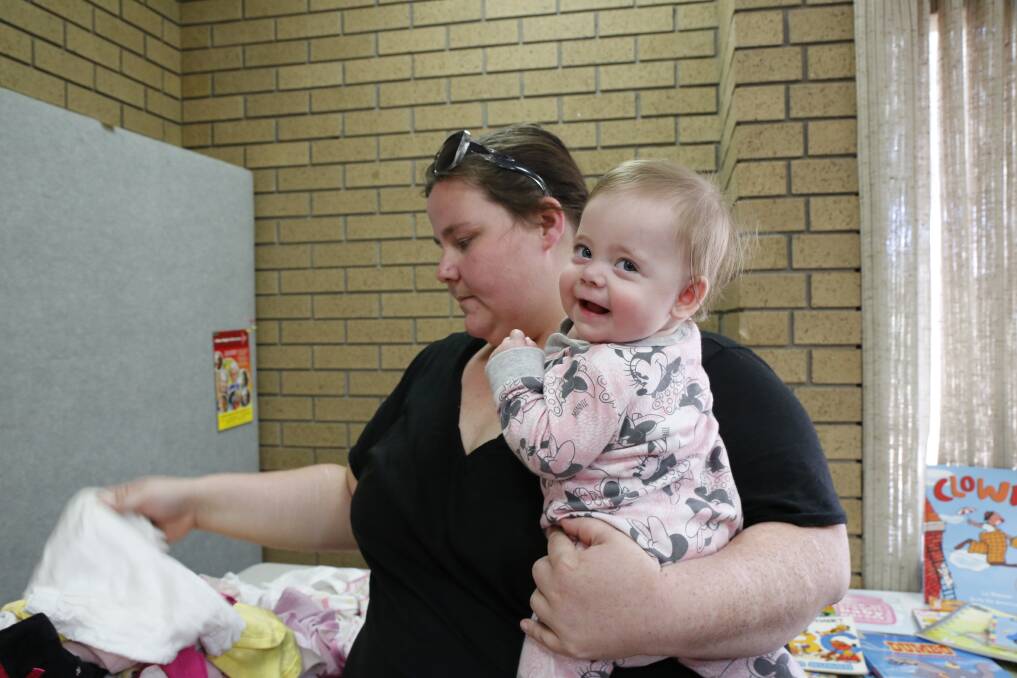 HELPING HAND: Emily Brown flashes a smile at the camera while her mother, Tania Brown, sifts through baby clothes at a pop-up op shop in Bendigo. Picture: EMMA D'AGOSTINO