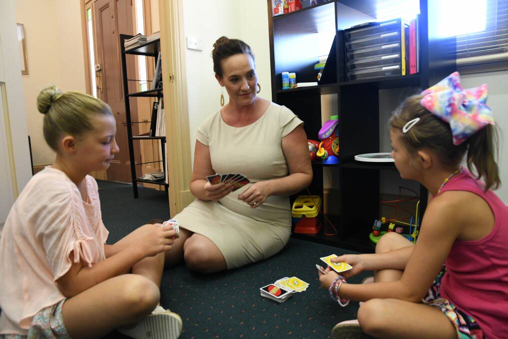 Taylah, 8, and Shaye, 7, with Dr Cara Tucker. The card game is an example of an icebreaker activity therapists can employ when working with children. Picture: EMMA D'AGOSTINO