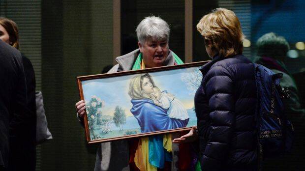 A woman holds a religious painting, as she waits in line outside Melbourne Magistrates Court. Photo: Justin McManus