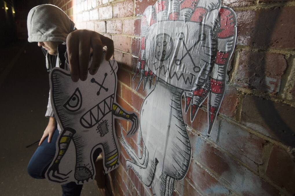 PASTE-UP: A local street artist with one of his distinctive, paper paste-up characters which can be quickly applied to a wall using a PVA glue mix. Picture: DARREN HOWE
