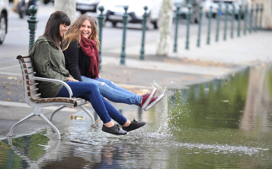 SPLASH: Patricia Garcia and Estefania Aura soak up the novelty of heavy rain in Bendigo in the middle of summer. Picture: NONI HYETT