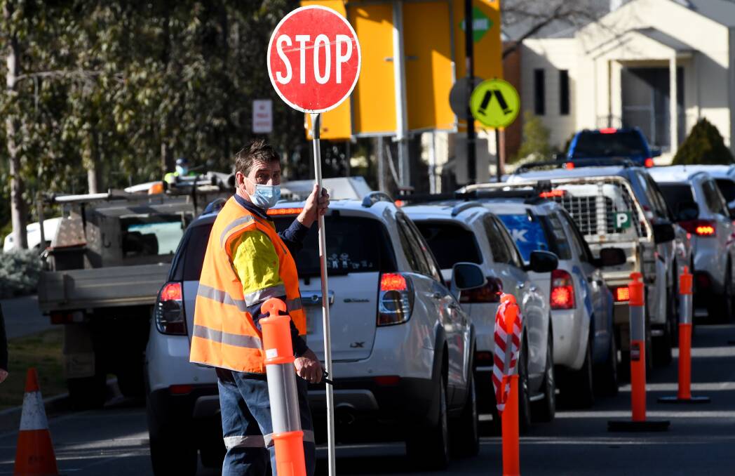 A worker helps direct traffic as a Bendigo testing centre grapples with long lines of cars.