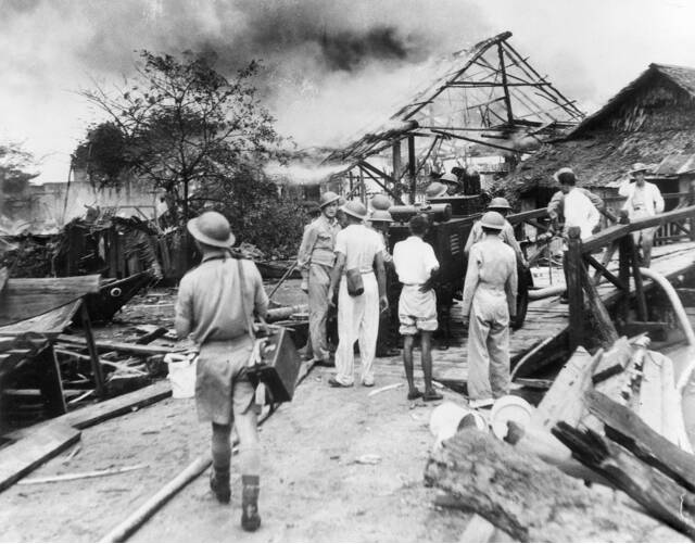 Soldiers and civilian defence groups survey the damage after Japan air raids in a village in Singapore. Picture: UNKNOWN BRITISH ARMY PHOTOGRAPHER courtesy of the AUSTRALIAN WAR MEMORIAL