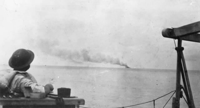 A sailor watches the Empress of Asia burn following an attack by Japanese dive bombers. Picture: Courtesy of the AUSTRALIAN WAR MEMORIAL