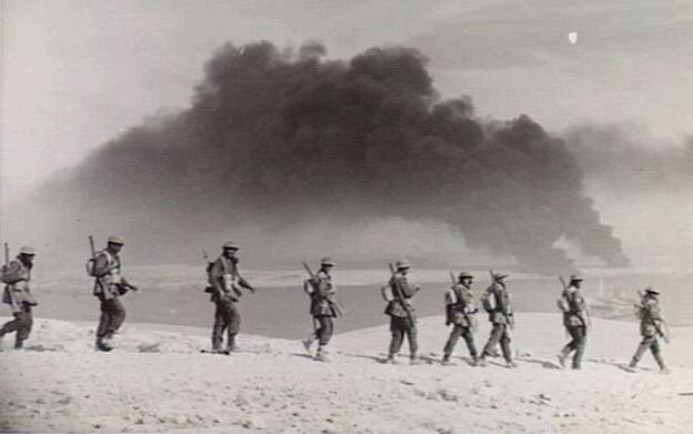 Australian infantry prepare to enter Tobruk on 23 January, 1941, which is covered by the plum of thick, dark smoke from burning oil tanks. Picture: JAMES FRANCIS HURLEY and the AUSTRALIAN WAR MEMORIAL