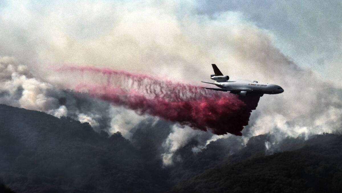High toll: A firefighting DC-10 makes a fire retardant drop over a wildfire in the mountains near Malibu Canyon Road in Malibu, California on Sunday. Picture: Richard Vogel, AP

