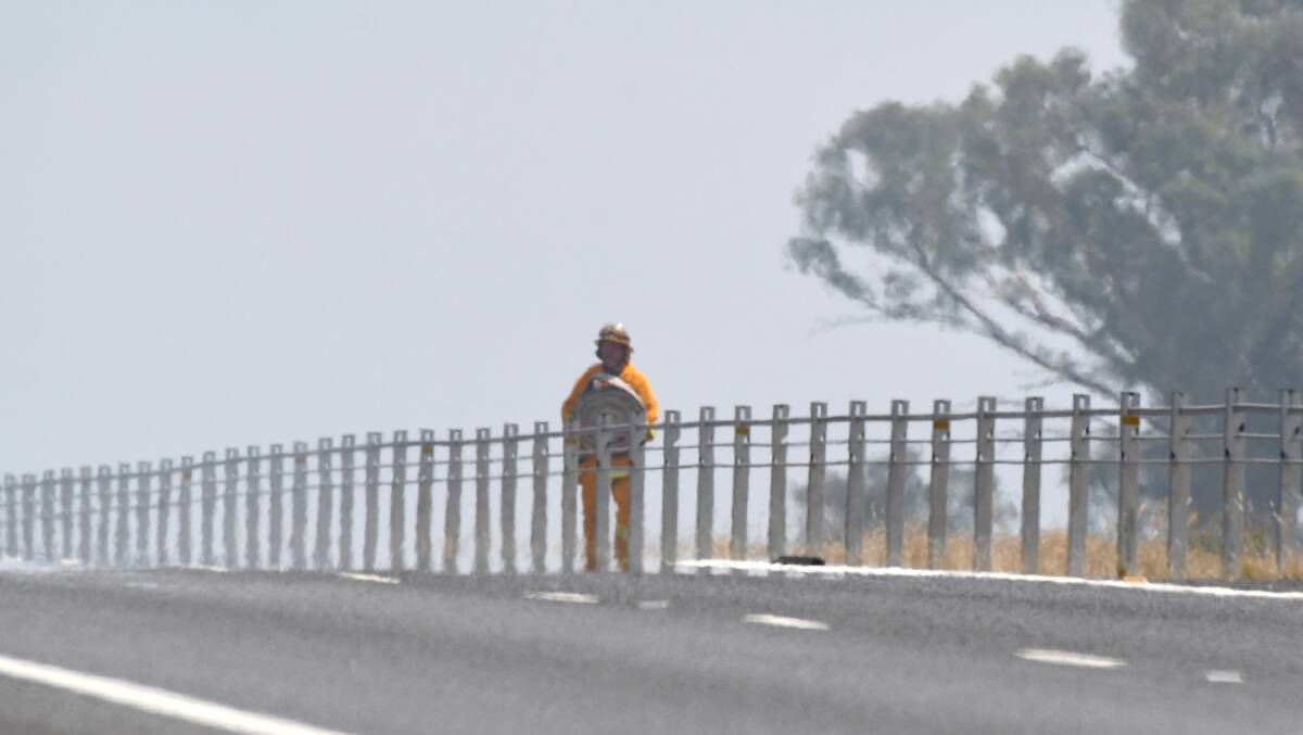WATER: A firefighter carrying a hose during a grass fire in February is pictured behind the wire rope barriers on the Calder Highway. Picture: NONI HYETT