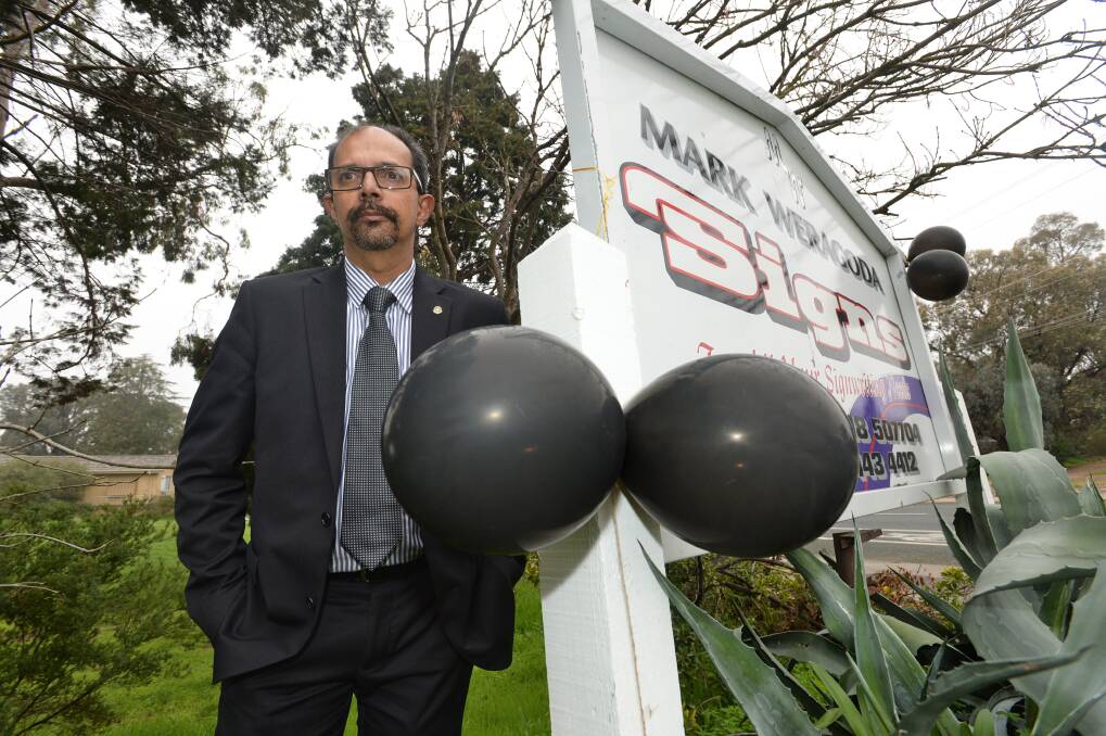Councillor Mark Weragoda standing next to his business sign, to which protesters affixed black balloons. Picture: JUSTIN McMANUS