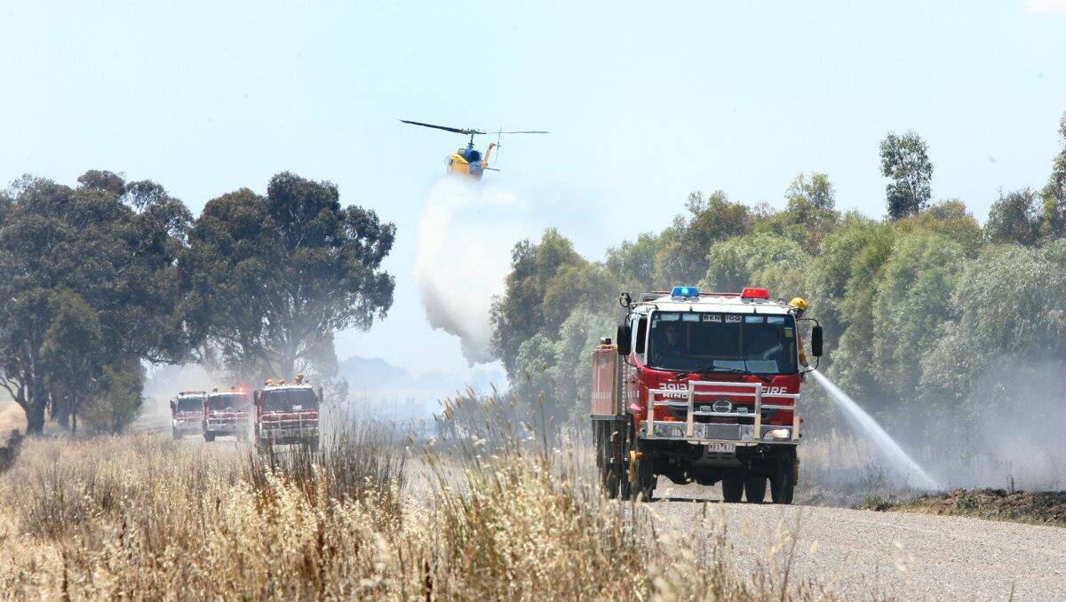 AFTERMATH: Firefighters, assisted by a waterbombing helicopter, mop up after yesterday’s crop fire at Raywood. Picture: PETER WEAVING